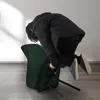 A person in a black coat is interacting with a green chair, which is tipped over. Voir les images du produit