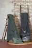Two blankets and two pillows with a deer motif are displayed in a rustic setting with a brick wall and a wooden ladder. Produktbild-Vorschau