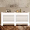 A white radiator cover with horizontal slats is displayed in a room with a painting above it and decorative items on top. Náhľad obrázku produktu