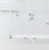 A close-up view of a white roman blind with a subtle butterfly pattern. Produktbild-Vorschau