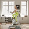 A woman is exercising on a stationary bike in a bright, modern room with large windows. Produktbild-Vorschau