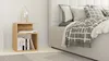 A bedside table with books and a lamp next to a bed with pillows and a blanket. Podgląd zdjęcia produktu