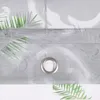 A close-up view of a gray sheer curtain with a green leaf pattern and a metal grommet. Produktbild-Vorschau
