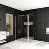 A modern bathroom with black herringbone tiles, a glass shower enclosure with a gold frame, and a white vanity. Produktbild-Vorschau