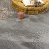 A close-up view of a fluffy gray rug with a yellow cushion and a candle on it. Produktbild-Vorschau