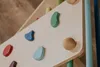 A close-up view of a wooden climbing triangle with colorful climbing holds attached. Produktbild-Vorschau