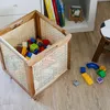 A storage basket filled with colorful building blocks sits on a wooden floor next to a small stool and some scattered blocks. Produktbild-Vorschau