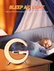 A baby sleeping in a crib next to a crescent-shaped lamp with a digital clock and a phone charging on it. Produktbild-Vorschau