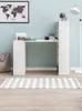 A modern white desk with a bookshelf attached to one side, set against a light blue wall. A world map poster hangs on the wall above the desk. A striped rug is on the floor in front of the desk. Anteprima dell’immagine prodotto