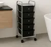 A roll container with five black drawers and a silver top is shown in a bathroom setting next to a wooden vanity and a white bathtub. Produktbild-Vorschau