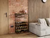 A wine rack filled with wine bottles and glasses is placed next to a sofa in a room with a brick wall. Podgląd zdjęcia produktu