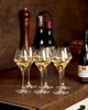 Six wine glasses filled with a light-colored liquid are arranged on a brown countertop. In the background, there are bottles and a pepper grinder. Produktbild-Vorschau