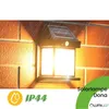 A solar-powered outdoor wall lamp is mounted on a brick wall, with light illuminating the surrounding area and rain effects shown. Produktbild-Vorschau