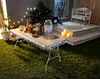 An outdoor evening party scene with a table set for a gathering, decorated with string lights. Produktbild-Vorschau