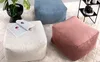 Three corduroy poufs are arranged on a textured rug. One is white, one is light blue, and one is pink. A plant in a black pot is visible on the left, and a shelf unit with a camera is on the right. Náhľad obrázku produktu