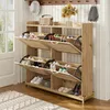 A wooden shoe cabinet with multiple flip-down compartments and an open storage shelf, placed in an entryway or hallway. Náhľad obrázku produktu