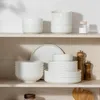 A collection of white ceramic dishes and bowls neatly arranged on a wooden shelf. Produktbild-Vorschau