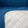 A close-up of a quilted blue sofa cover with a white quilted underside. Produktbild-Vorschau