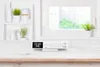 A white under-cabinet radio with a digital display sits on a light-colored wooden countertop in front of a blurred window. Produktbild-Vorschau