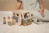 A child's hand is visible, interacting with a wooden toy camper van and accessories on a fluffy rug. Náhled obrázku produktu
