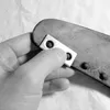 A hand is holding a metal plate with two holes over a black object with metal studs. Anteprima dell’immagine prodotto