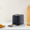 A dark gray Tefal toaster sits on a white countertop with toast and toast crumbs nearby. Produktbild-Vorschau