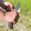 Hands holding a knife and sharpening a piece of wood outdoors. Produktbild-Vorschau