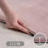 A hand is shown pressing down on the edge of a pink rug, with a close-up inset showing the thickness of the rug. Produktbild-Vorschau