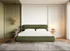 A bedroom scene with a green upholstered bed as the focal point, flanked by bedside tables with lamps and decorative items. The room features a mix of green and white walls, wooden flooring, and a large rug. Produktbild-Vorschau