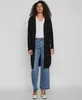 A woman is standing and modeling a black cardigan over a white t-shirt and blue jeans. Produktbild-Vorschau