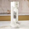 A white soda maker with a bottle of carbonated water is shown on a marble countertop. Podgląd zdjęcia produktu