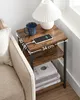 A bedside table with a lamp, mug, and phone charging, next to a couch. Náhled obrázku produktu