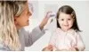 A woman is holding a thermometer to a child's forehead. Voir les images du produit