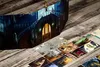 A board game setup on a wooden table, featuring a screen with a grand staircase illustration and several cards laid out. Podgląd zdjęcia produktu