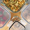 Four glass food storage containers filled with different food items are arranged on a wooden surface. Produktbild-Vorschau