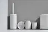 A collection of white bathroom accessories arranged on a shelf against a gray wall. Produktbild-Vorschau