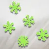 Several green snowflake-shaped cutouts are scattered on a textured white surface, with soft shadows cast by them. Podgląd zdjęcia produktu
