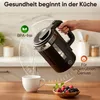 A hand pouring hot water from a black electric kettle into a white mug, with a bowl of berries in the foreground. Produktbild-Vorschau