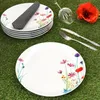 A stack of plates and a single plate are arranged on a green grassy surface, with cutlery, a wine glass, and a poppy flower. Produktbild-Vorschau