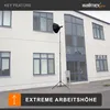 A lamp stand with a light modifier is set up outdoors in front of a modern building. Podgląd zdjęcia produktu