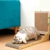 A cat is lying on a cat scratching post next to a teal couch. Podgląd zdjęcia produktu