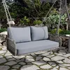 A garden swing set with cushions is placed on a stone patio, surrounded by lush greenery and a stone wall. Podgląd zdjęcia produktu