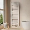 A white towel radiator is mounted on a light beige wall next to a large window. A small wooden stool with a folded towel and some toiletries sits in front of the window. Náhľad obrázku produktu