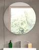 A round mirror is mounted on a gray tiled wall above a white sink. A green soap dispenser, a silver faucet, and a yellow bar of soap are on the sink. Produktbild-Vorschau