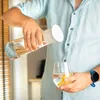 A person is pouring water from a glass carafe into a glass with lemon slices. Produktbild-Vorschau