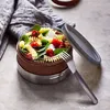 A round lunchbox filled with pasta salad, placed on a textured surface next to a folded napkin and a fork. Anteprima dell’immagine prodotto
