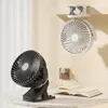 Two clip-on fans are displayed, one black on a table and one white hanging from a shelf, with an open book and an electrical outlet visible. Produktbild-Vorschau