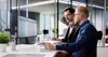 Two men working in an office environment, looking at a computer monitor displaying a spreadsheet. Produktbild-Vorschau