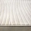 A close-up view of a textured white rug with a curved line pattern, resting on a grey wooden floor. Anteprima dell’immagine prodotto