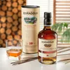 A bottle of Edradour 10 Year Old Highland Single Malt Scotch Whisky, a glass of whisky, and its cylindrical packaging are displayed on a table. Produktbild-Vorschau